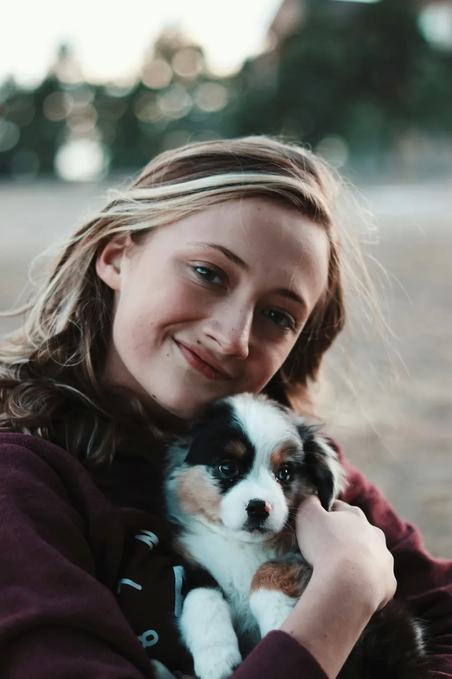 A smiling young woman holding a fluffy black, white and tan puppy close to her chest